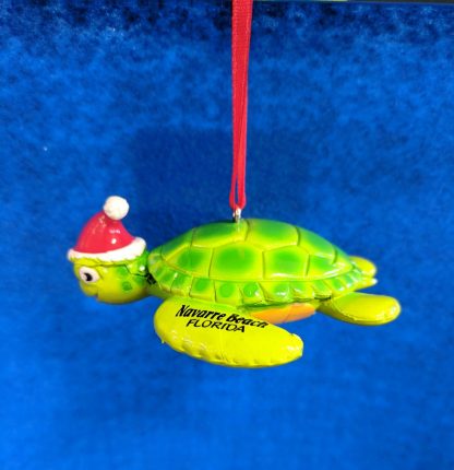 Sea turtle ornament made from durable rubber. Bright green on the shell that fades to yellow on bottom. Wearing a Santa Hat on head. Navarre Beach Florida is painted on the front left flipper.
